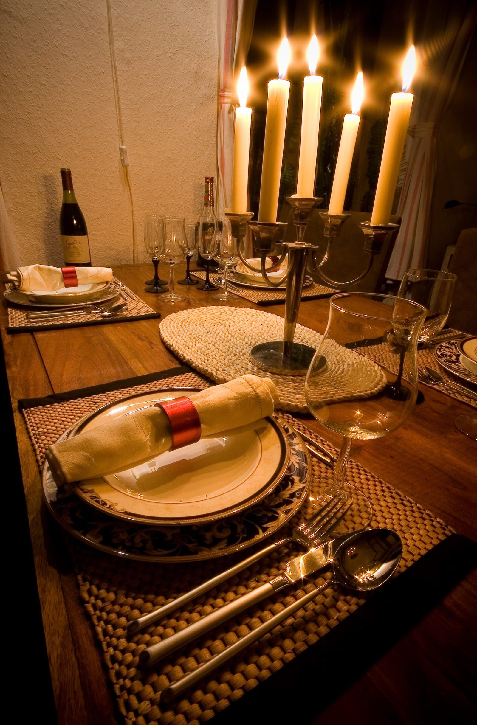 Gedeckter Holztisch mit Tellern, Stoffservietten, Weingläsern und einem Kerzenleuchter mit brennenden Kerzen