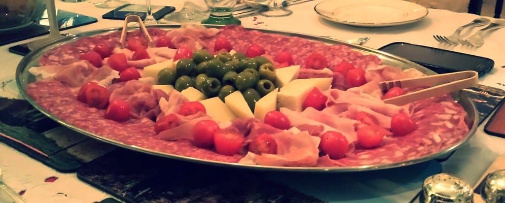 Große Platte mit Salami, Schinken, grünen Oliven, Käsewürfeln und Kirschtomaten auf einem gedeckten Tisch