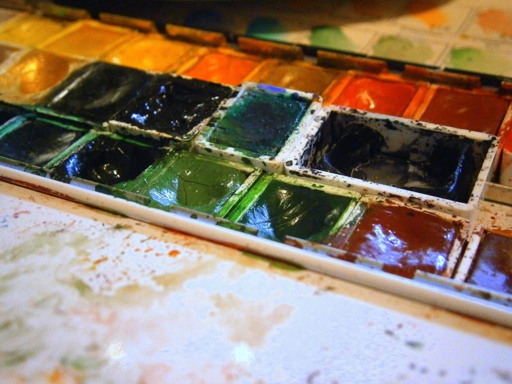 Nahaufnahme eines benutzten Aquarellkastens mit grünen, blauen, roten und gelben Farbnäpfchen