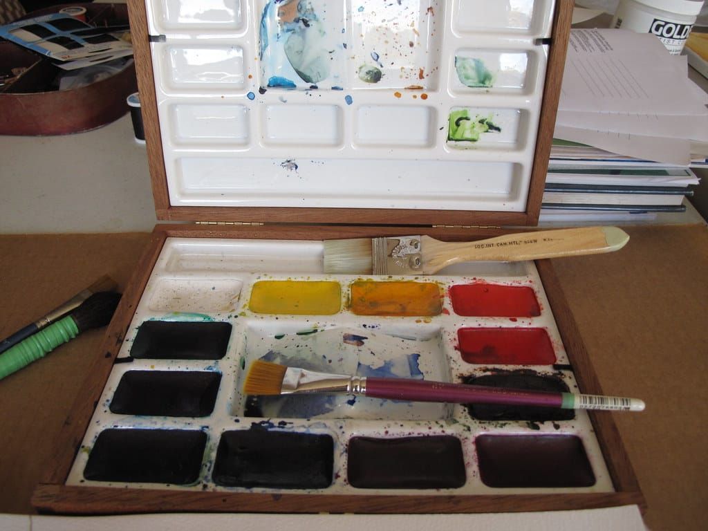Aufgeklappter Aquarellkasten aus Holz mit Farbnäpfchen, Mischflächen und zwei Pinseln