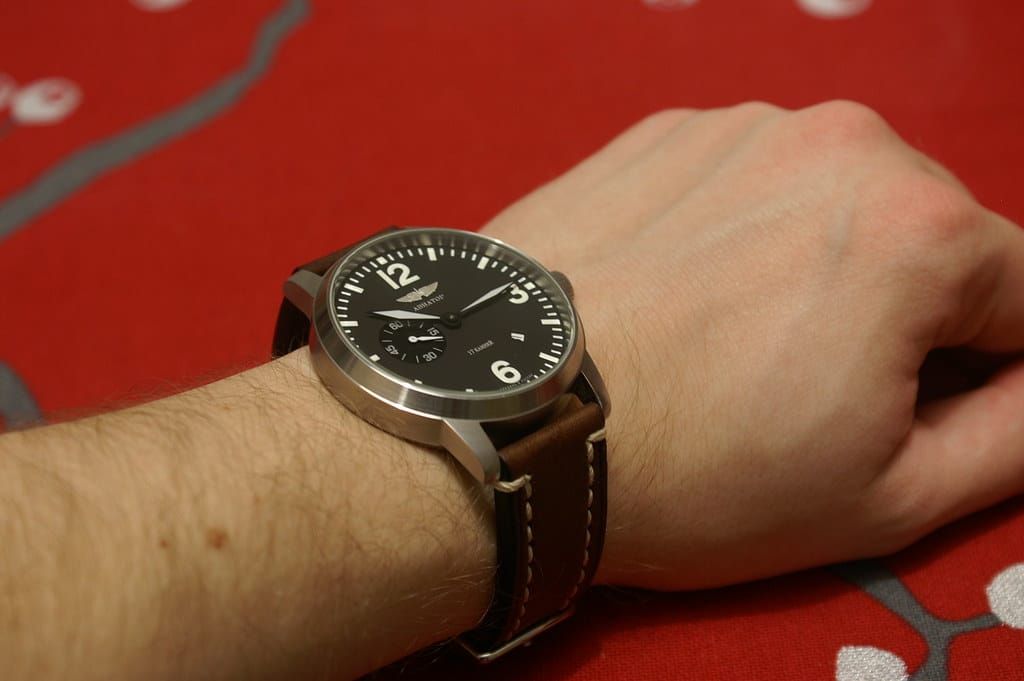 Handgelenk mit einer schlichten Armbanduhr mit schwarzem Zifferblatt, weißen Ziffern und braunem Lederarmband