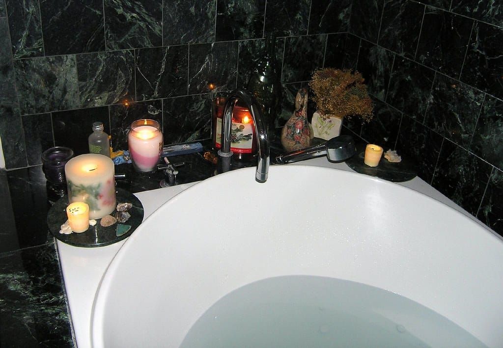 Badewanne mit warmem Wasser, auf dem Rand brennende Kerzen in verschiedenen Größen und getrocknete Blumen
