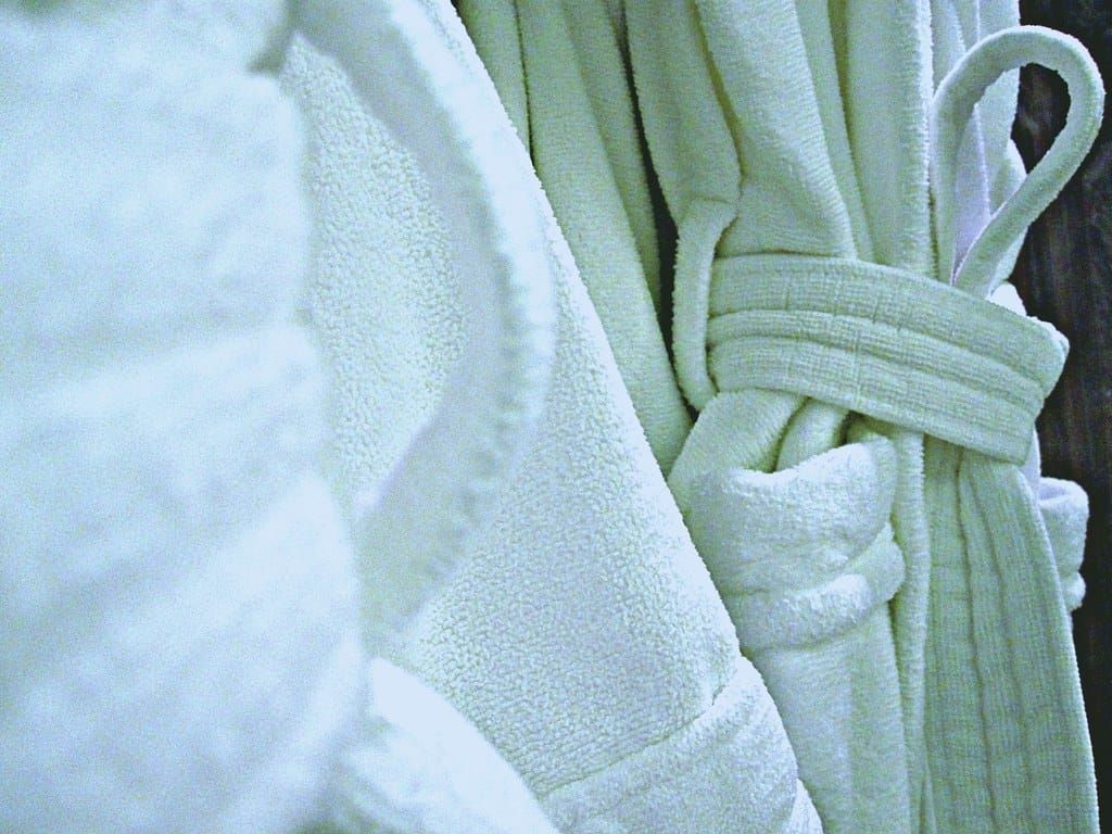 Zwei weiße, flauschige Bademäntel aus Frottee hängen nebeneinander, einer mit gebundenem Gürtel