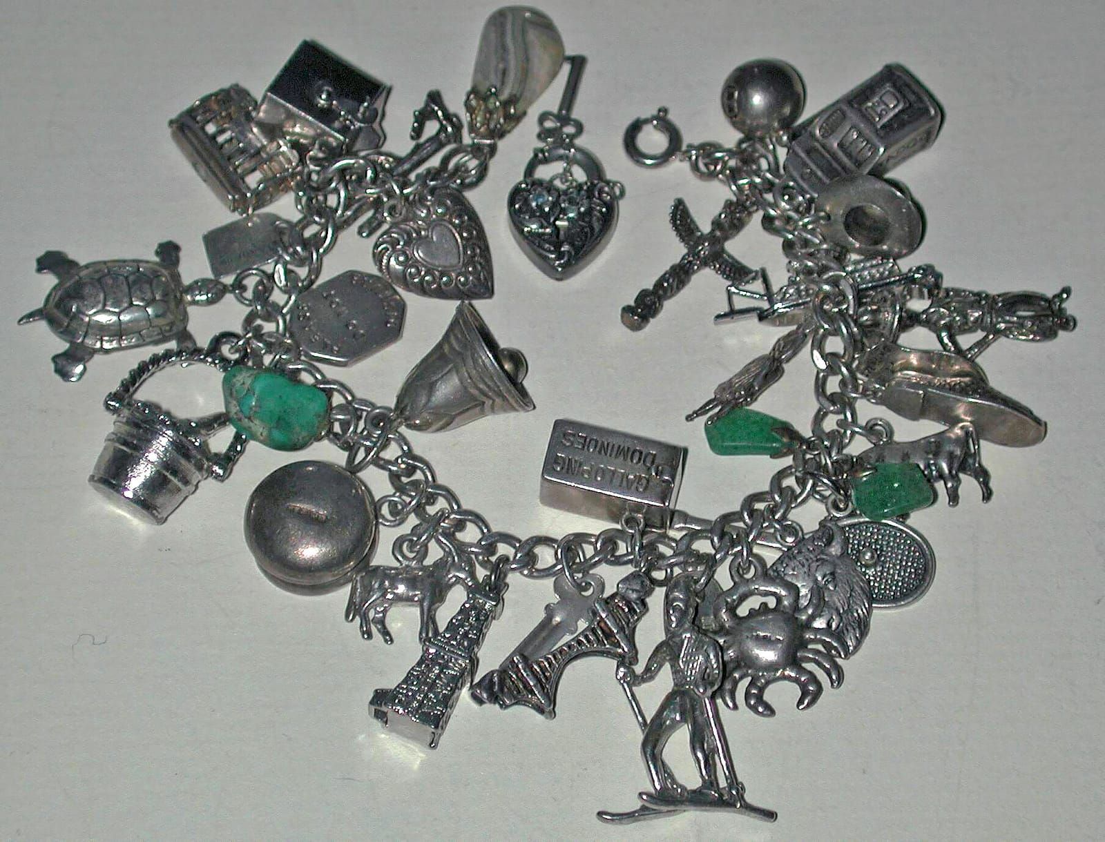 Silbernes Bettelarmband mit vielen Anhängern, darunter Herzen, Schildkröte, Glocke, Eimer und grüne Steine