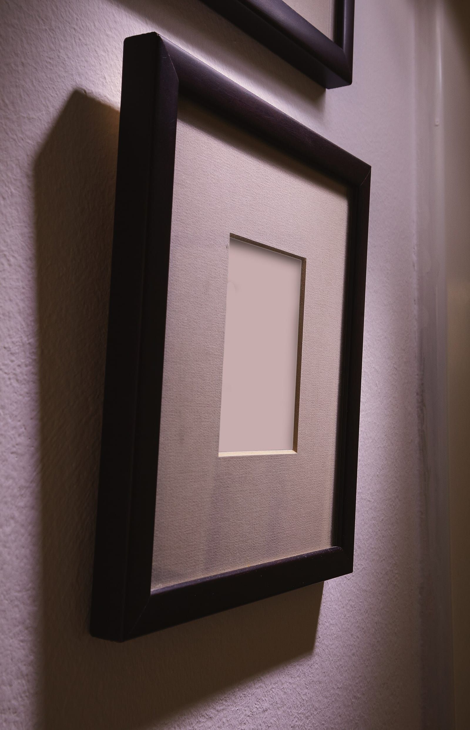 Leerer dunkler Holzrahmen mit hellem Passepartout an einer weißen Wand, schräg von der Seite fotografiert