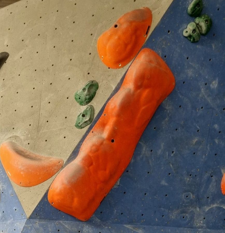 Kletterwand in Grau und Blau mit großen orangefarbenen und kleinen grünen Klettergriffen