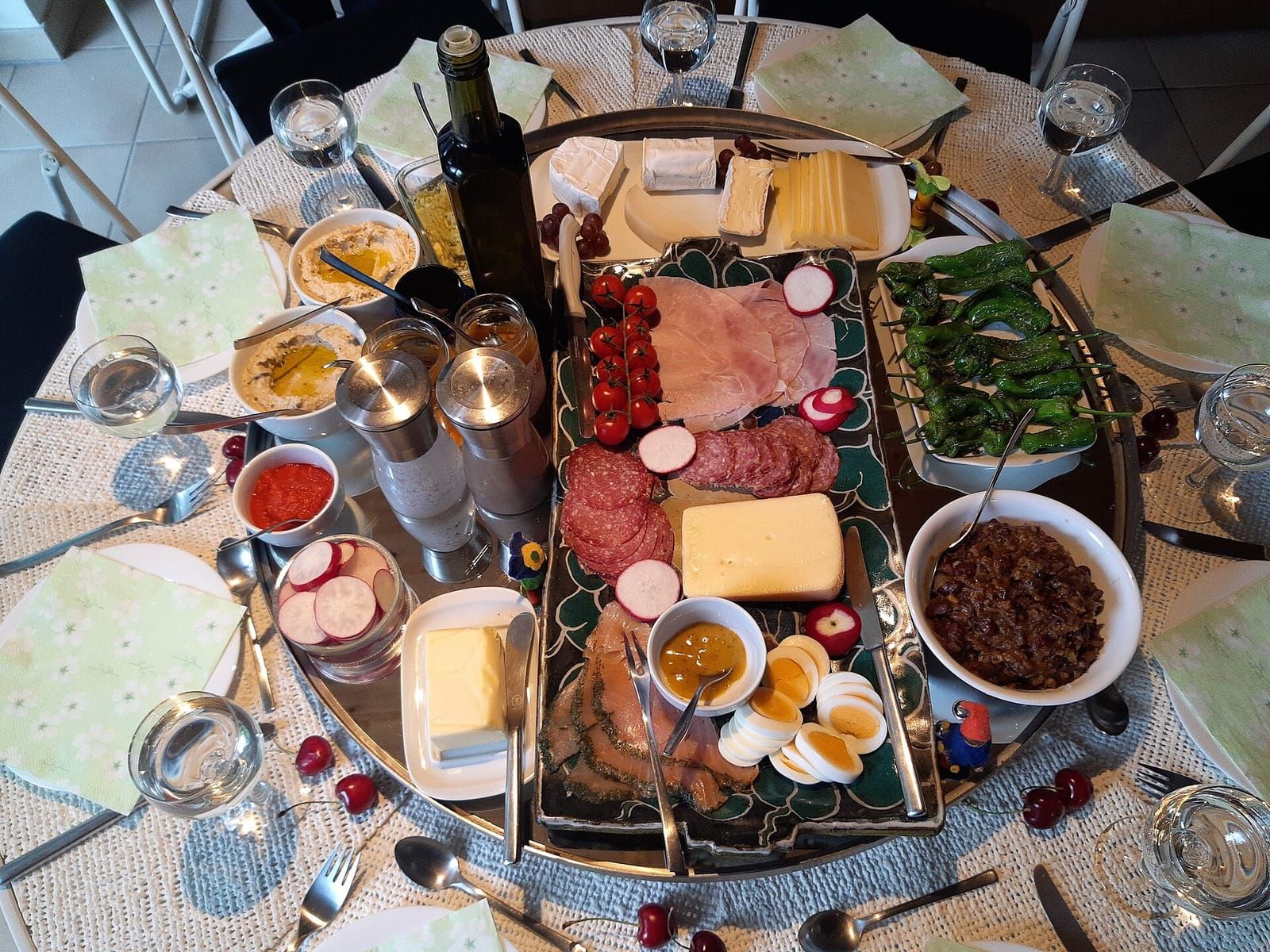 Runder, gedeckter Tisch mit Käse, Wurst, Lachs, Eiern, Radieschen, Dips und Wassergläsern von oben