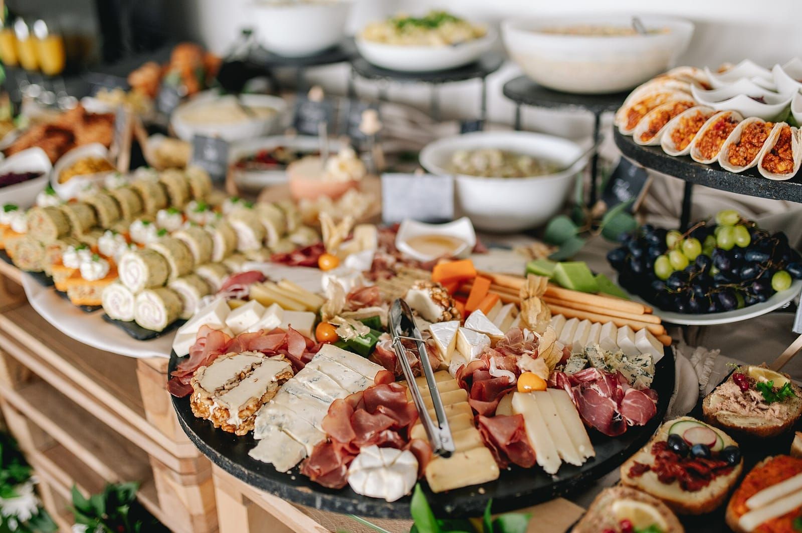 Buffettisch mit einer großen Platte aus Schinken und Käse, Wraps, Häppchen, Trauben und Salatschüsseln