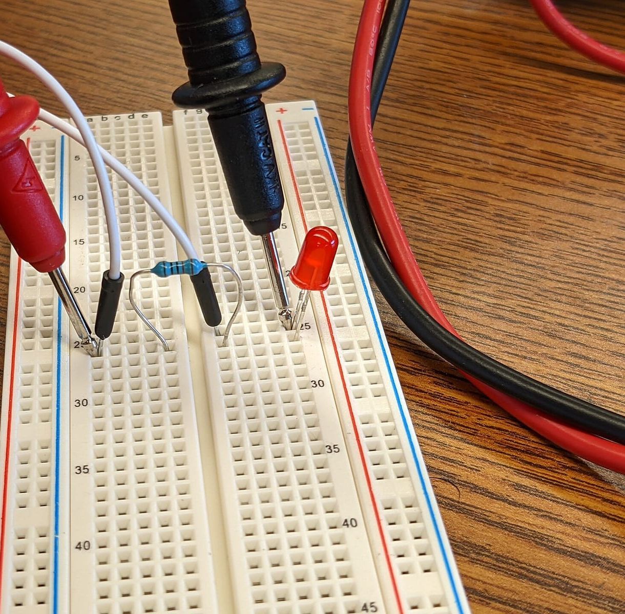 Steckbrett mit roter Leuchtdiode, Widerstand, weißen Kabeln und den Messspitzen eines Multimeters