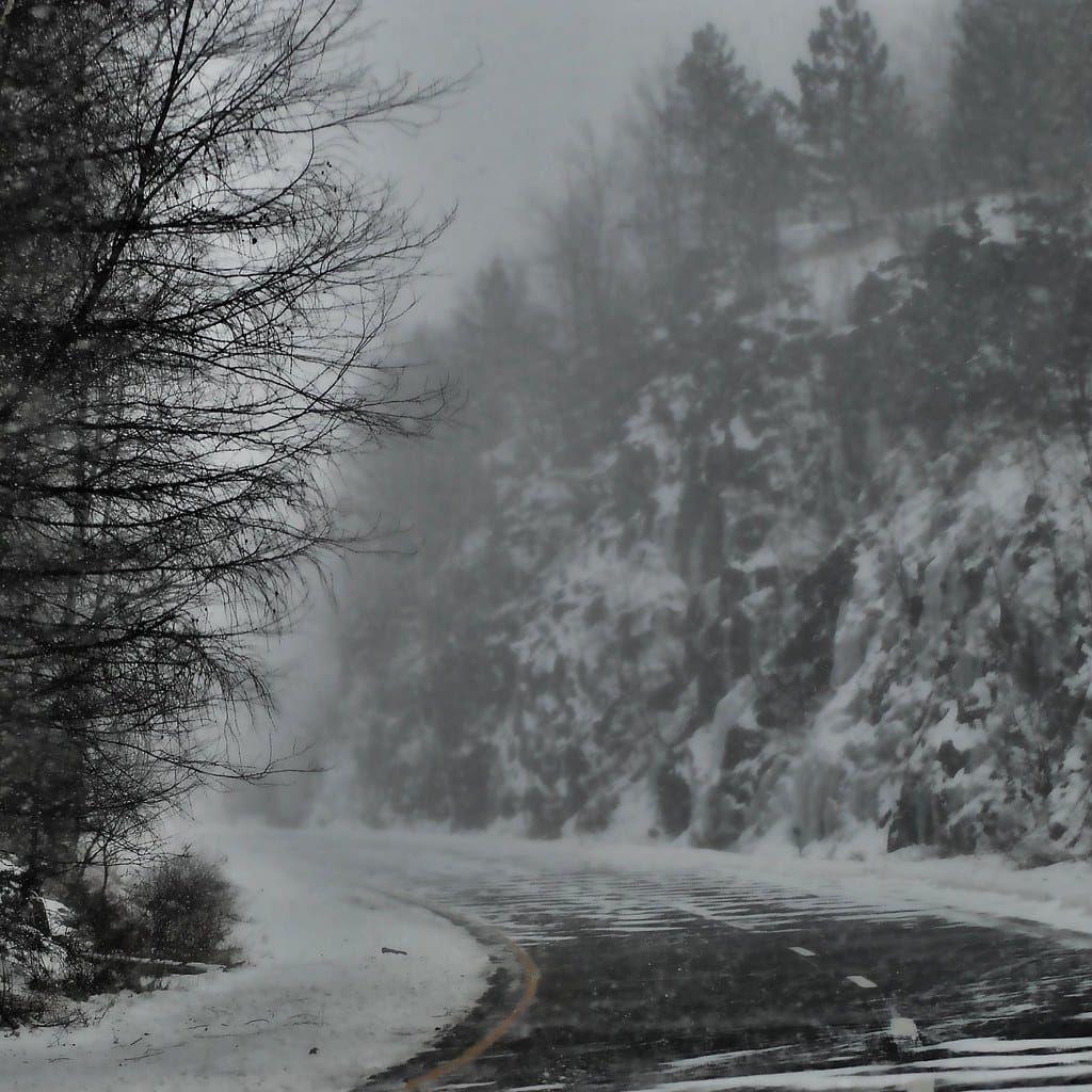 Kurvige Straße durch einen verschneiten Wald bei dichtem Schneetreiben