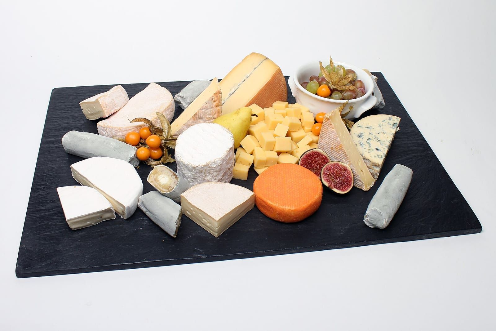 Schieferplatte mit verschiedenen Käsesorten, Feigen, Physalis, einer Birne und einer Schale Weintrauben
