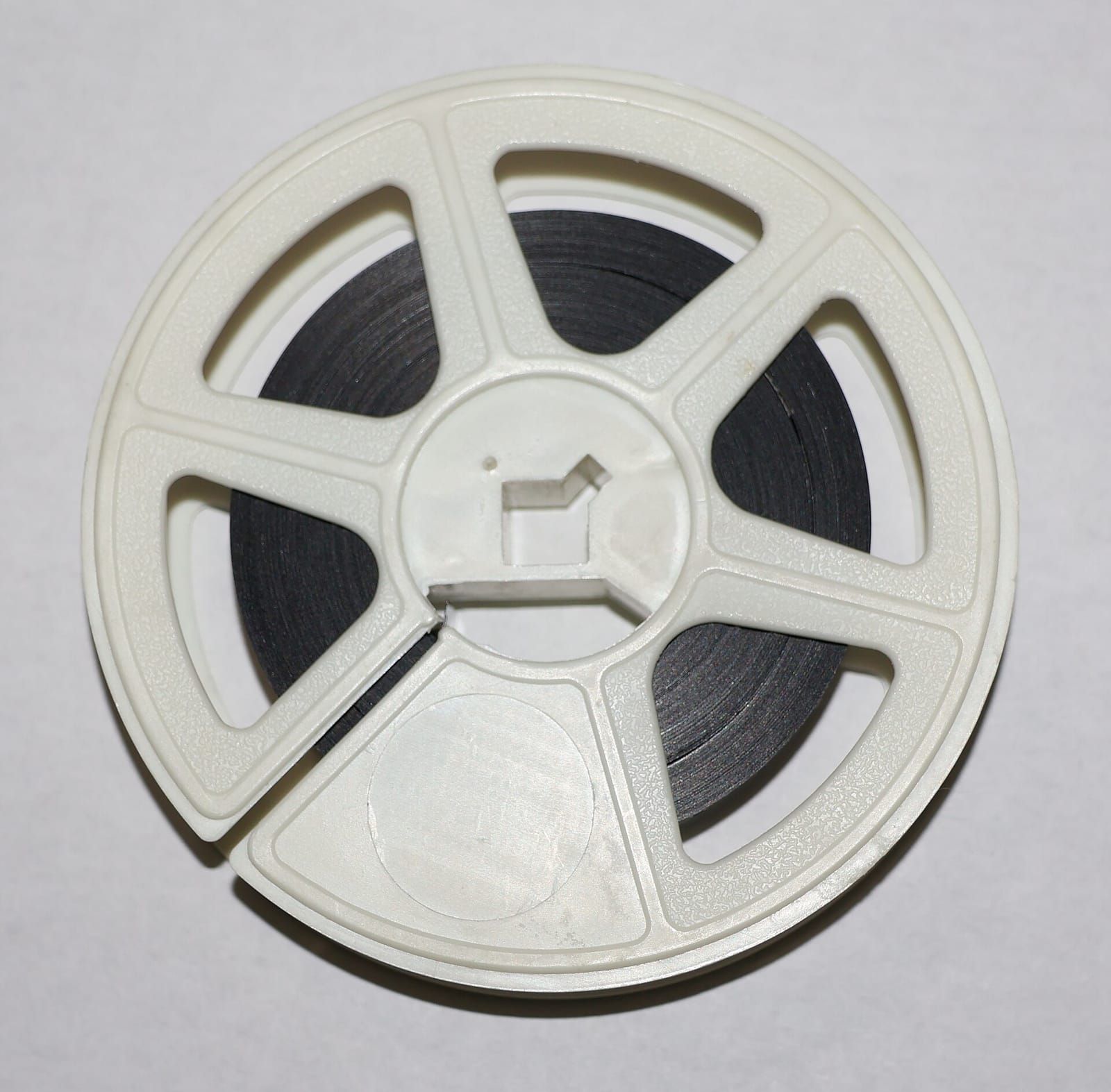 Kleine weiße Filmspule aus Kunststoff mit aufgewickeltem dunklem Film vor hellgrauem Hintergrund