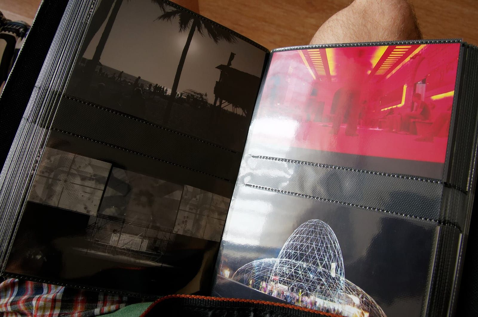 Aufgeschlagenes Fotoalbum mit Einstecktaschen, darin Fotos von Palmen am Strand, einem Festsaal und einer beleuchteten Kuppel