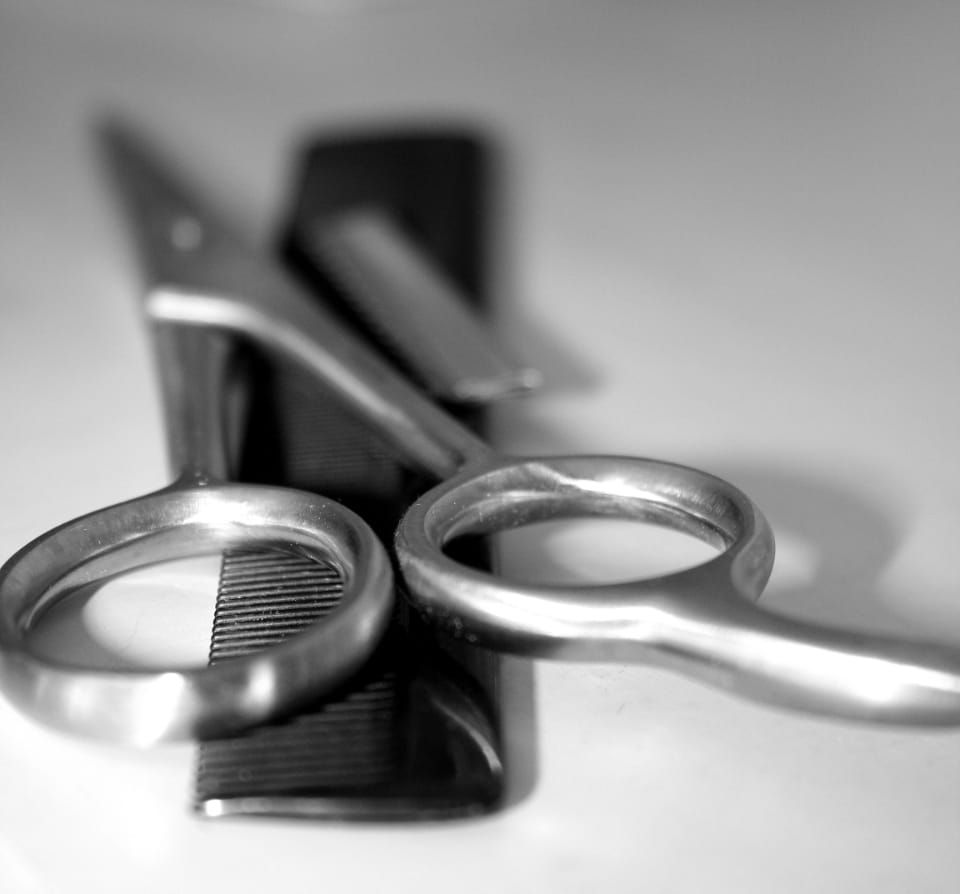 Schwarzweißaufnahme einer Friseurschere aus Metall, die auf einem schwarzen Kamm liegt