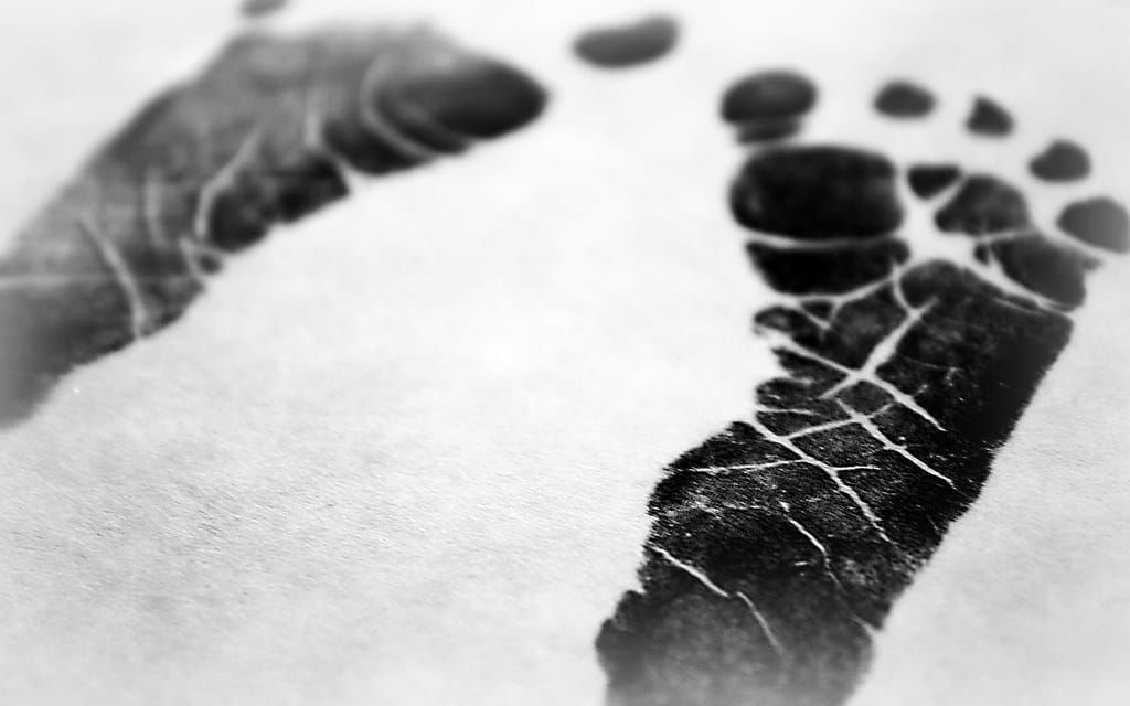 Schwarz-Weiß-Aufnahme von zwei kleinen Babyfußabdrücken in schwarzer Farbe auf weißem Papier