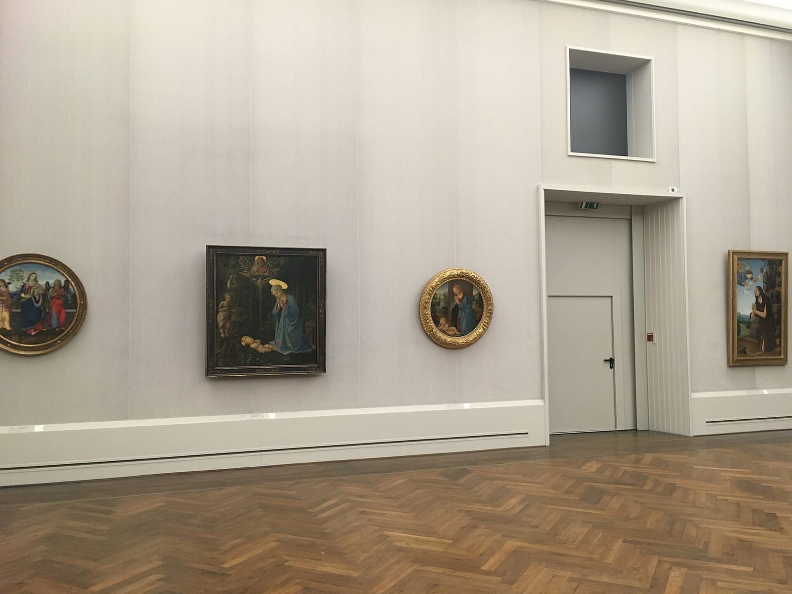 Ruhiger Museumssaal mit hellgrauen Wänden, Fischgrätparkett und mehreren Gemälden in Goldrahmen