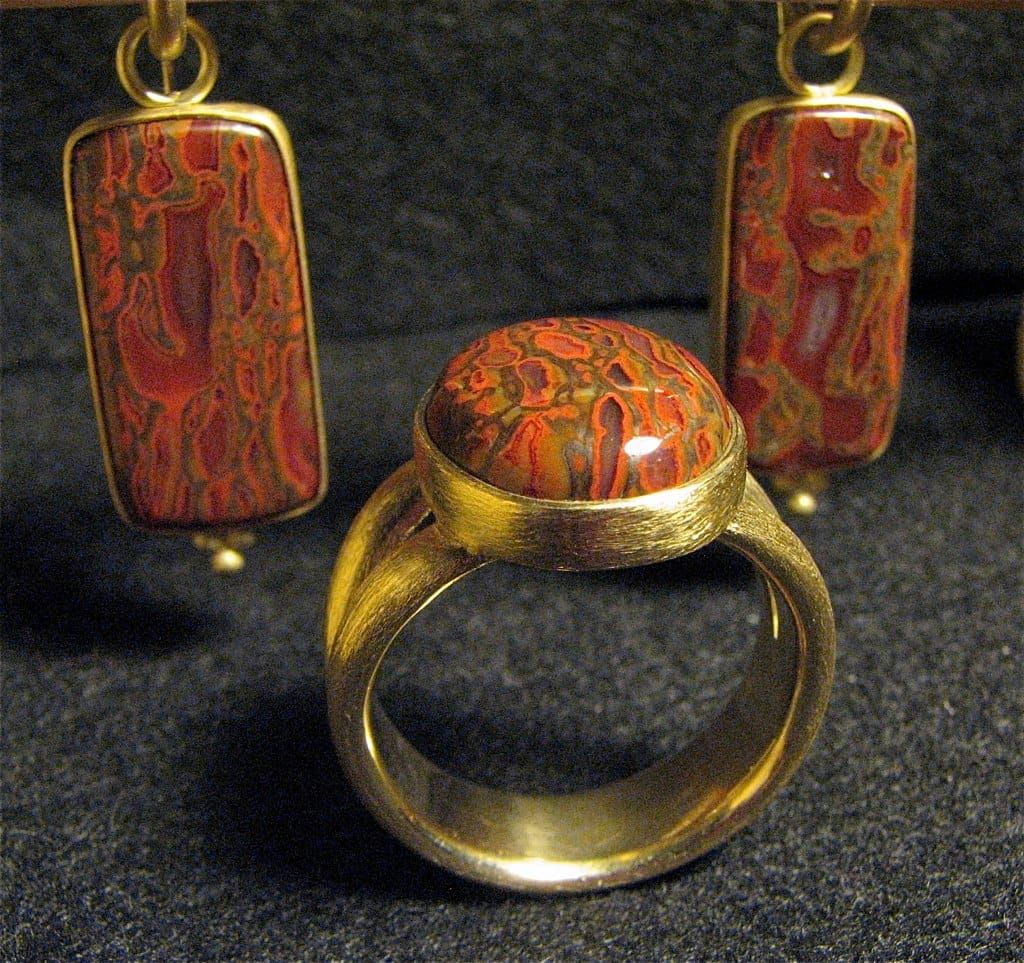 Handgefertigter Goldring mit ovalem rot-orange gemustertem Stein, dahinter passende Ohrhänger