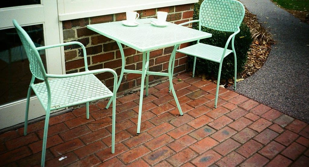 Kleiner mintgrüner Bistrotisch mit zwei Kaffeetassen und zwei Stühlen auf einer Terrasse aus Ziegelsteinen