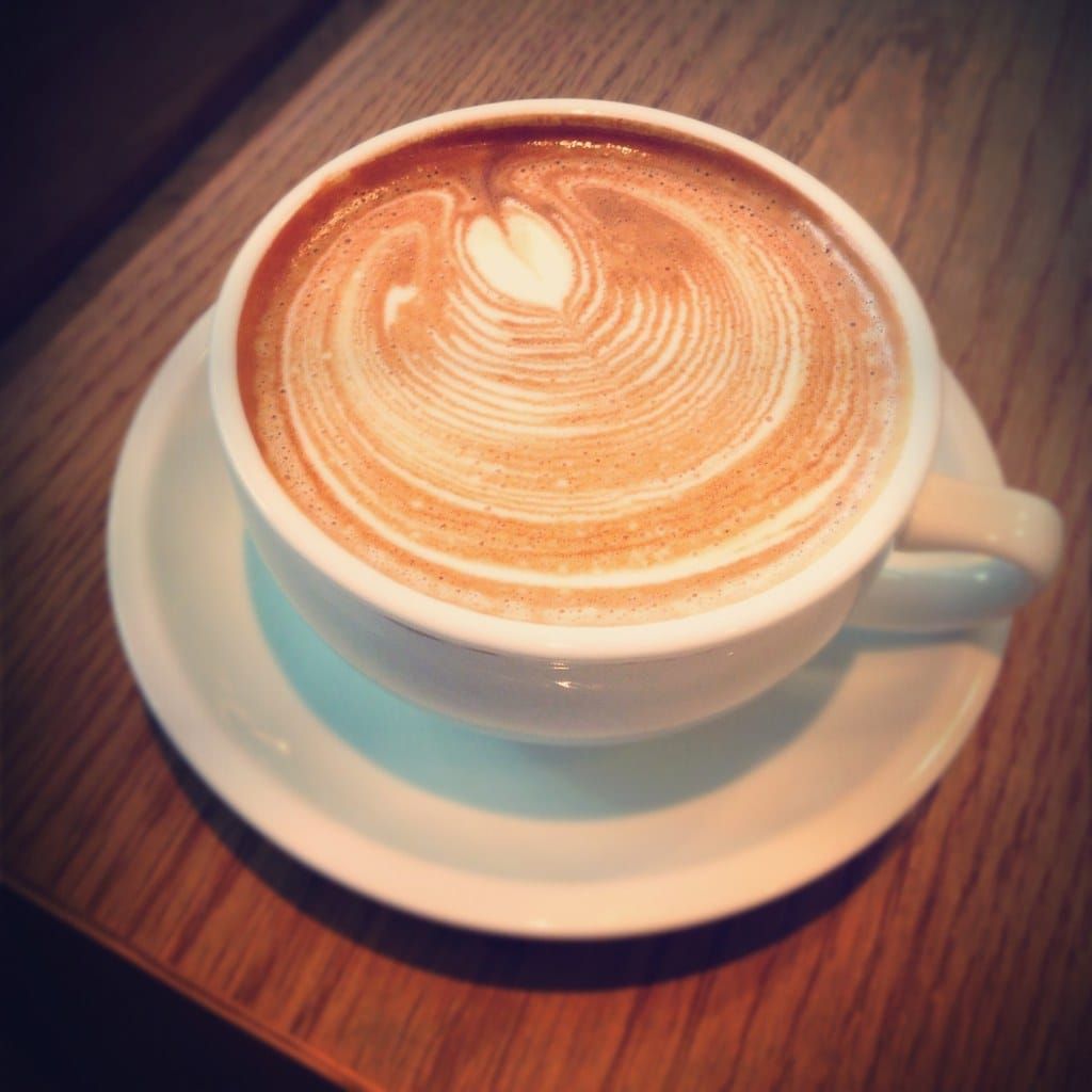 Weiße Tasse Cappuccino mit Milchschaum-Muster auf einer Untertasse, auf einem Holztisch