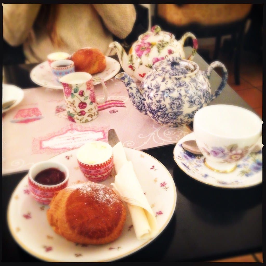 Kaffeetafel mit geblümtem Porzellan, zwei Teekannen, Scones mit Marmelade und Sahne auf einem Tisch