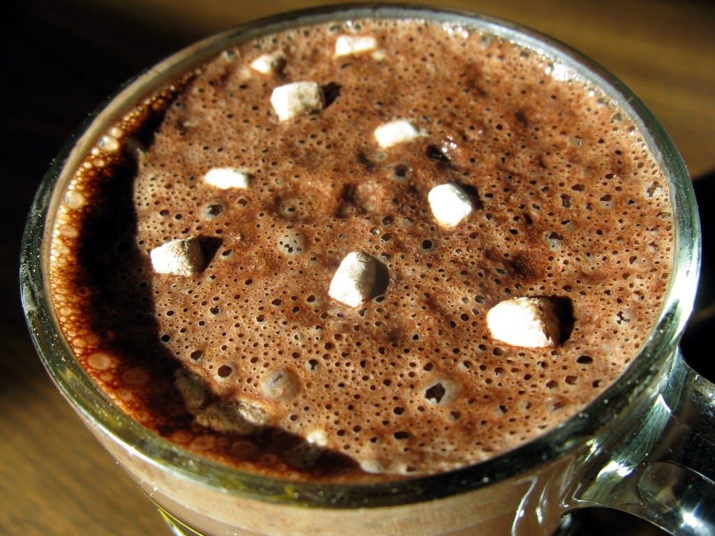 Glasbecher mit schaumigem heißem Kakao und kleinen Marshmallow-Stücken, von oben fotografiert