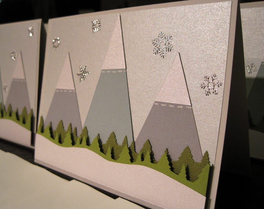 Handgemachte Weihnachtskarten mit Bergen aus Papier, grünen Tannen und silbernen Schneeflocken