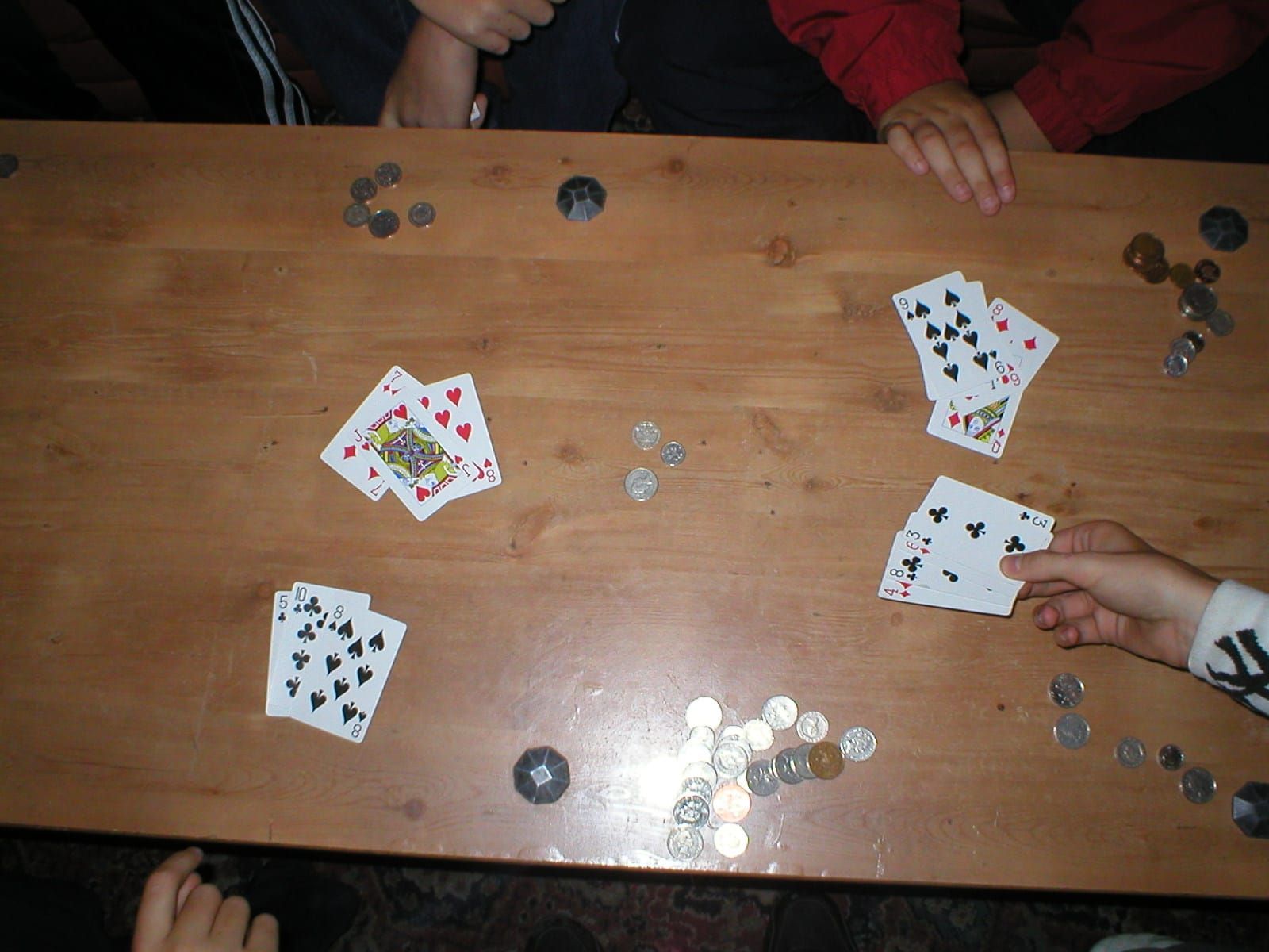 Spielkarten und Münzen liegen verteilt auf einem Holztisch, eine Hand hält mehrere Karten