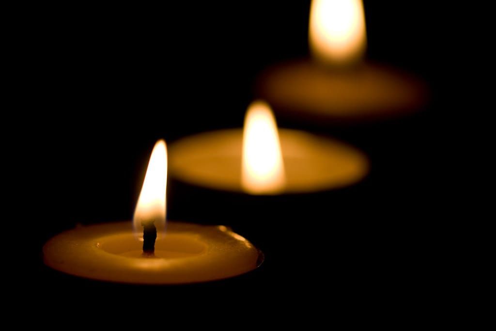 Drei brennende Kerzen mit warmem Licht vor schwarzem Hintergrund, die hinteren unscharf