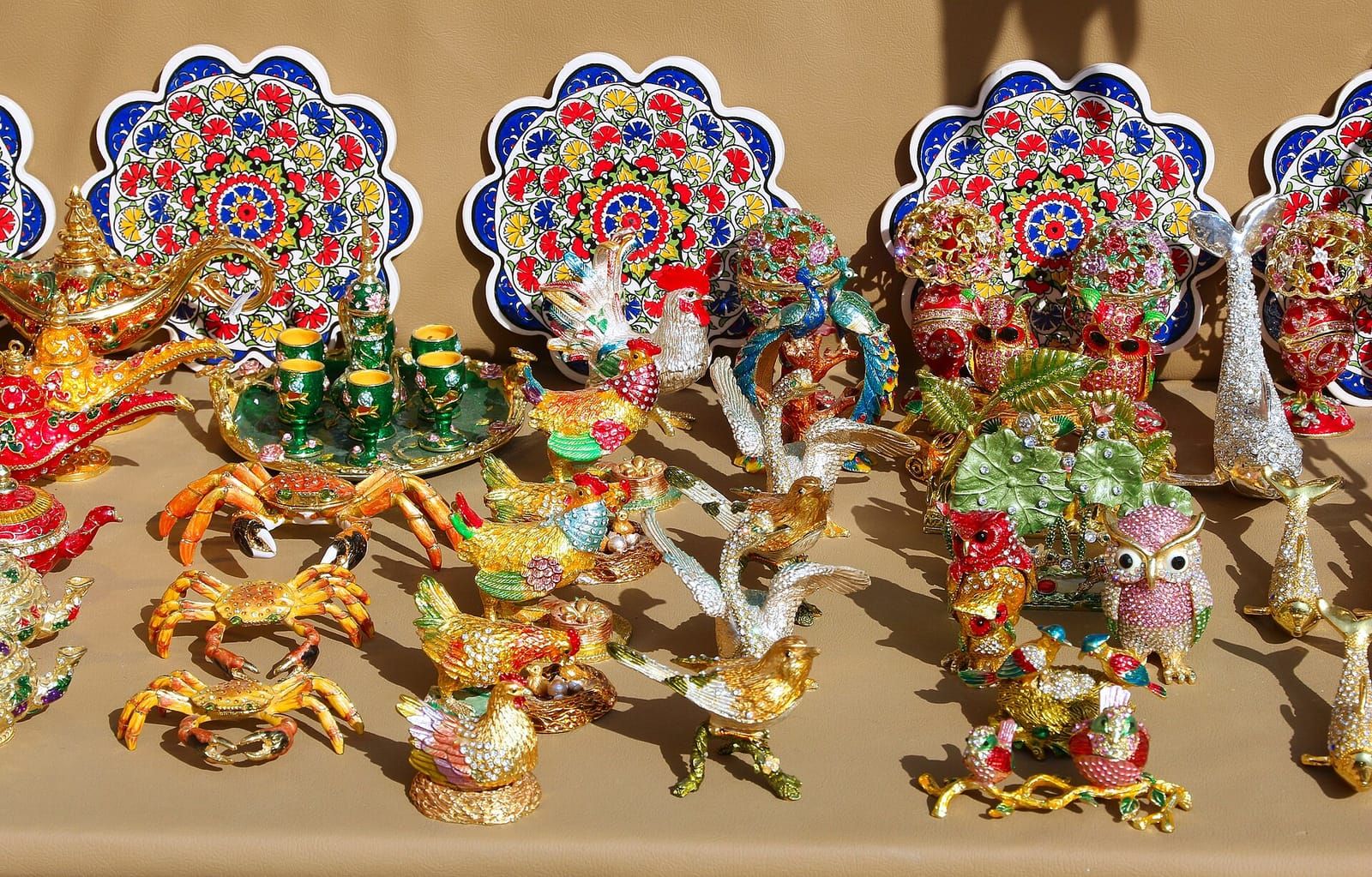 Viele glitzernde, bunt emaillierte Deko-Figuren wie Eulen, Krebse und Vögel vor verzierten Tellern