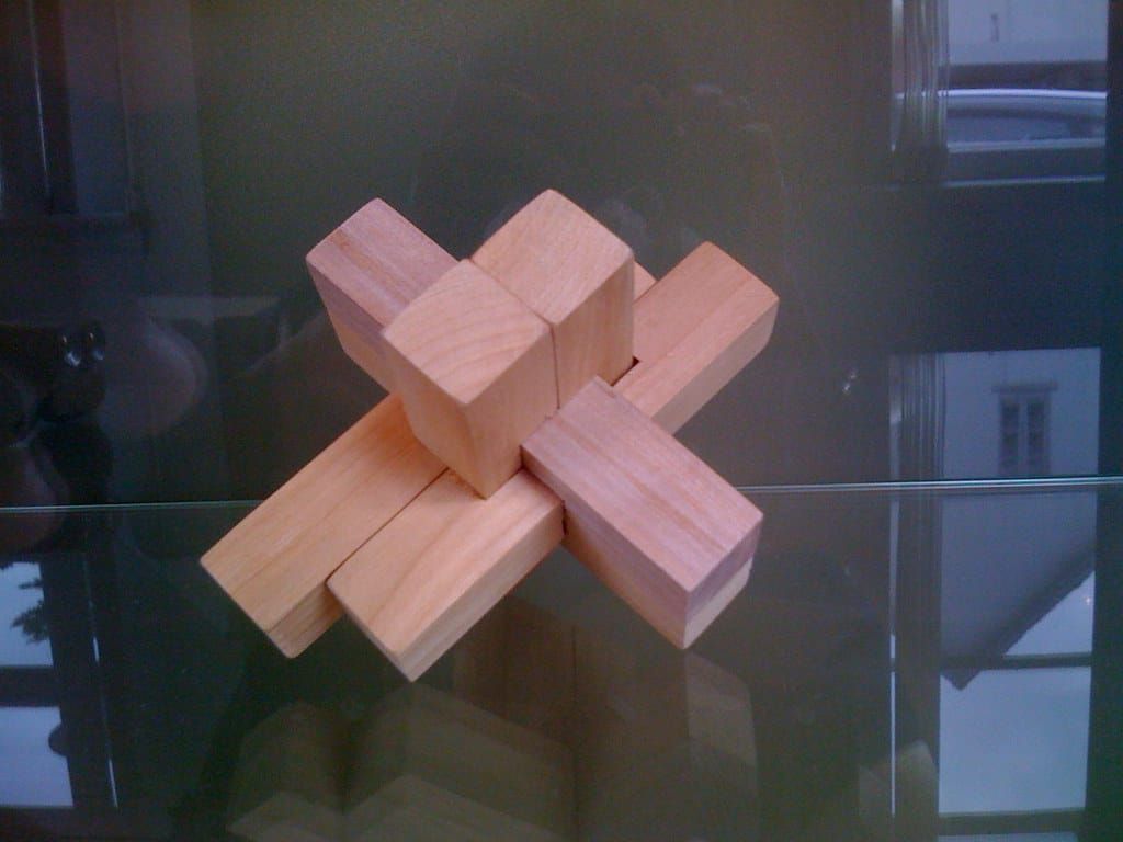 Zusammengesetztes Knobelspiel aus hellen Holzstäben in Kreuzform auf einer Glasplatte