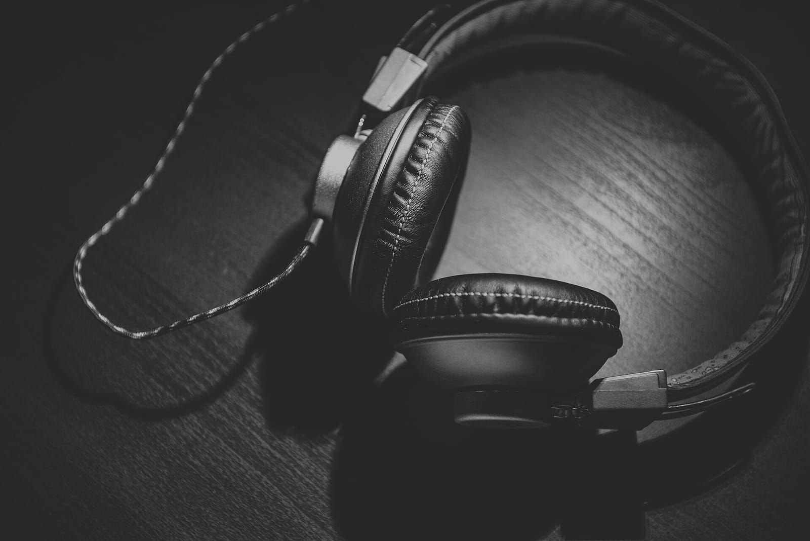 Schwarze Over-Ear-Kopfhörer mit Kabel auf einem dunklen Holztisch, Schwarz-Weiß-Aufnahme