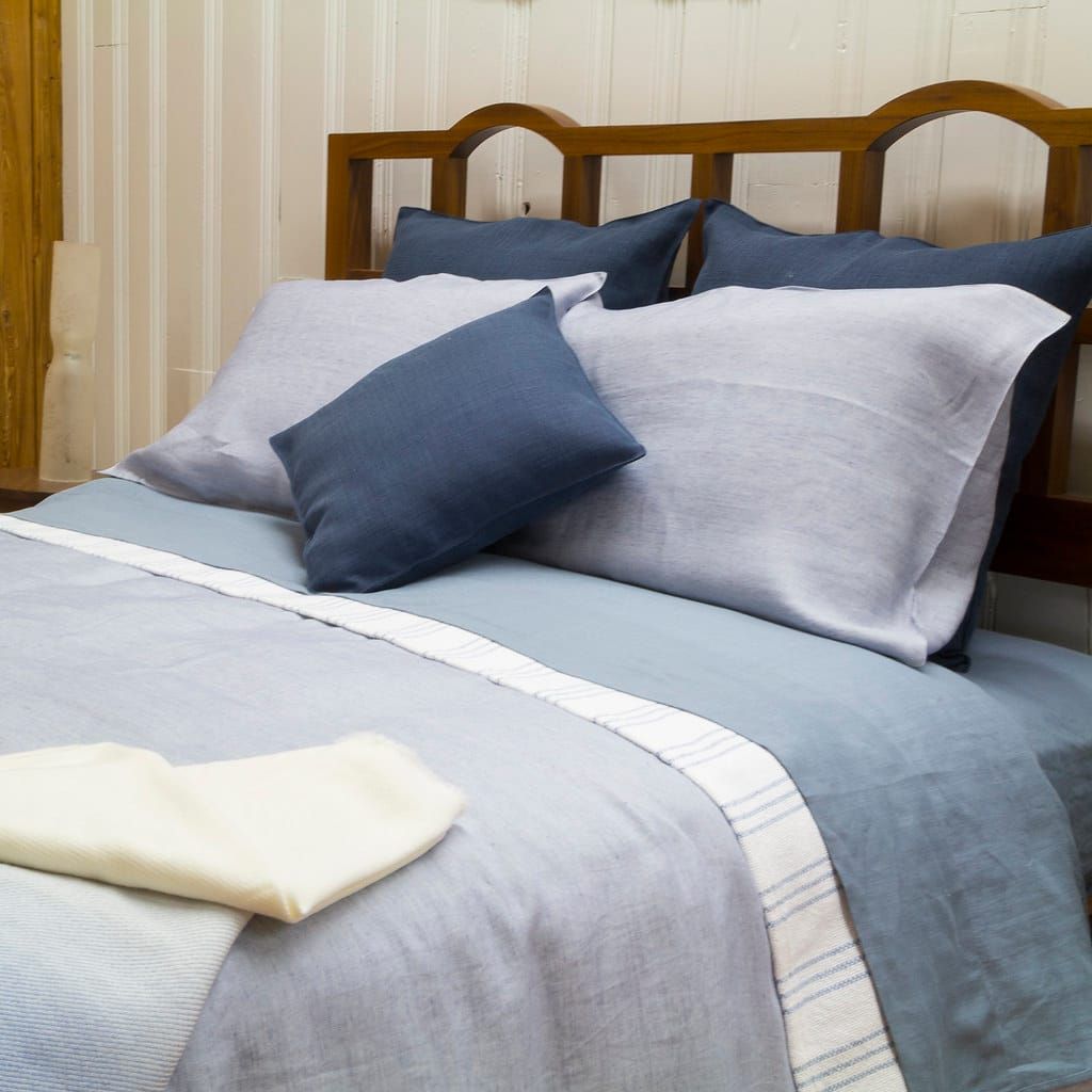 Bett mit Holzkopfteil und Bettwäsche aus Leinen in Hellblau und Graublau mit mehreren Kissen