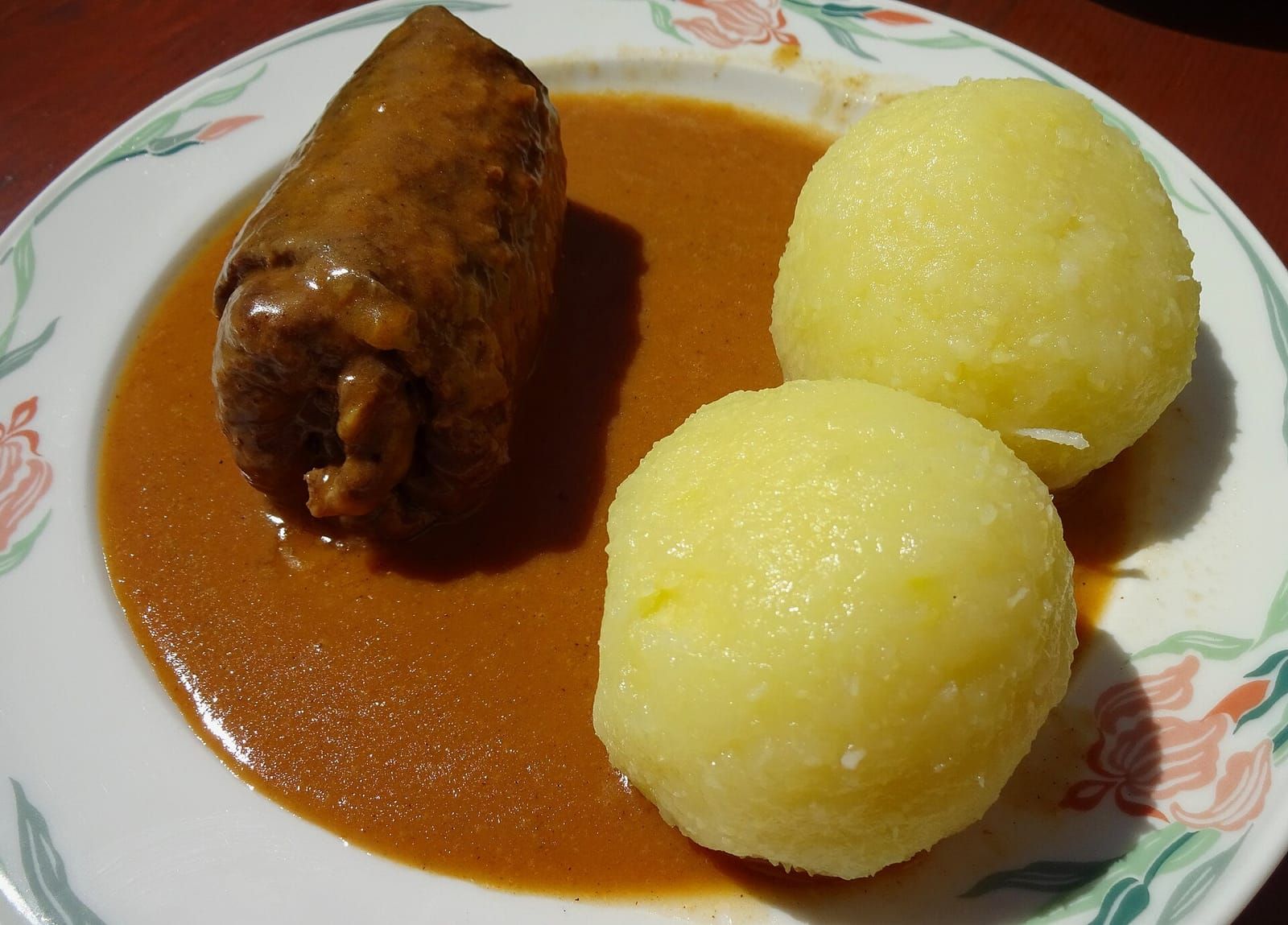 Teller mit einer Rinderroulade in dunkler Soße und zwei Kartoffelklößen auf geblümtem Porzellan