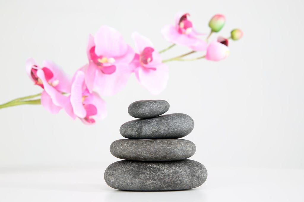 Gestapelte graue Massagesteine vor einer rosa Orchideenblüte auf hellem Hintergrund