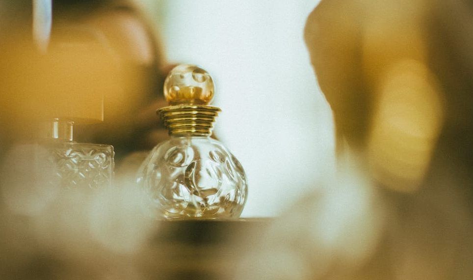Kleiner kugelförmiger Parfumflakon aus Glas mit goldenem Verschluss vor warm leuchtendem, unscharfem Hintergrund