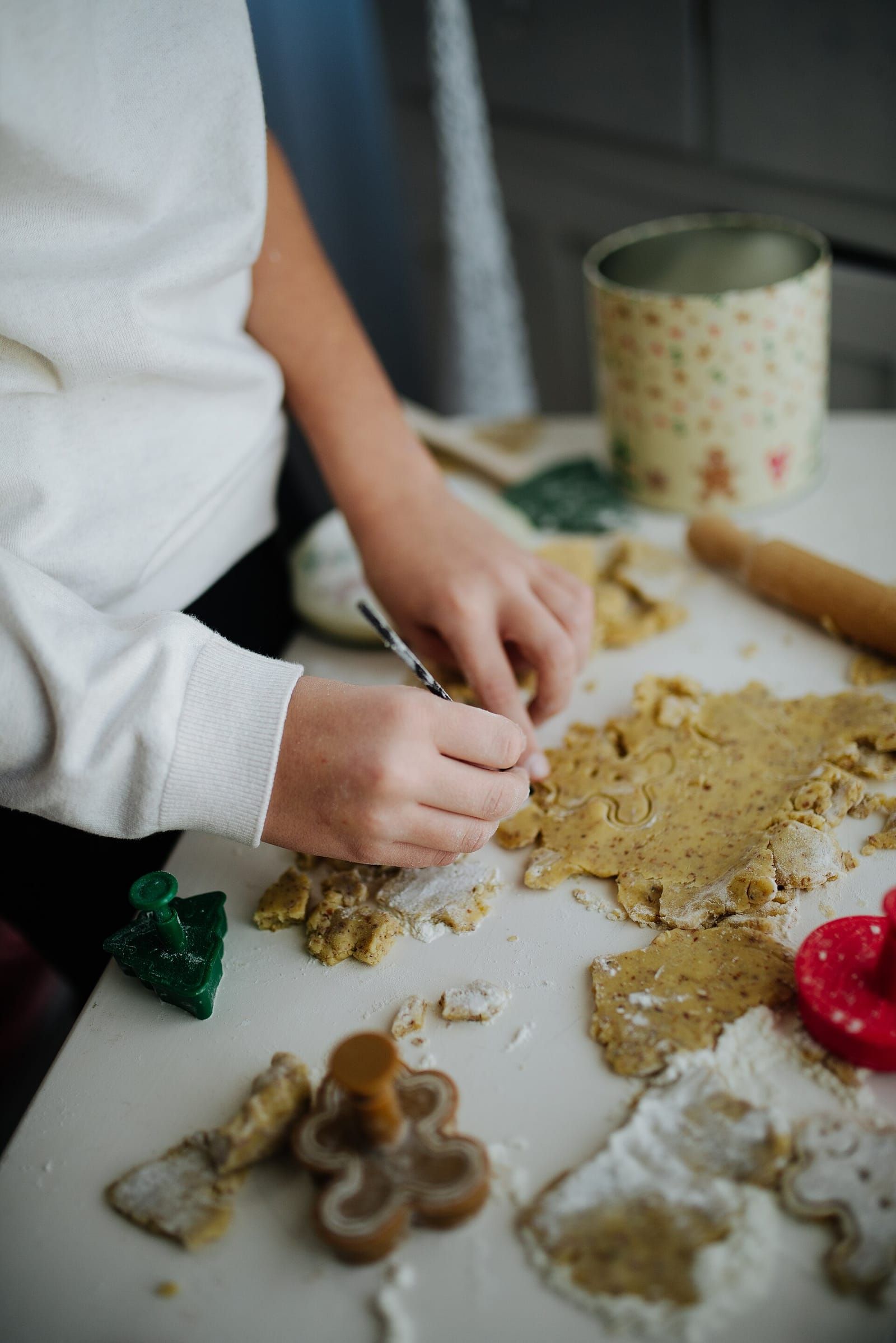 Kinderhände stechen auf einer bemehlten Arbeitsplatte Plätzchen aus, daneben Ausstecher, Nudelholz und eine Keksdose