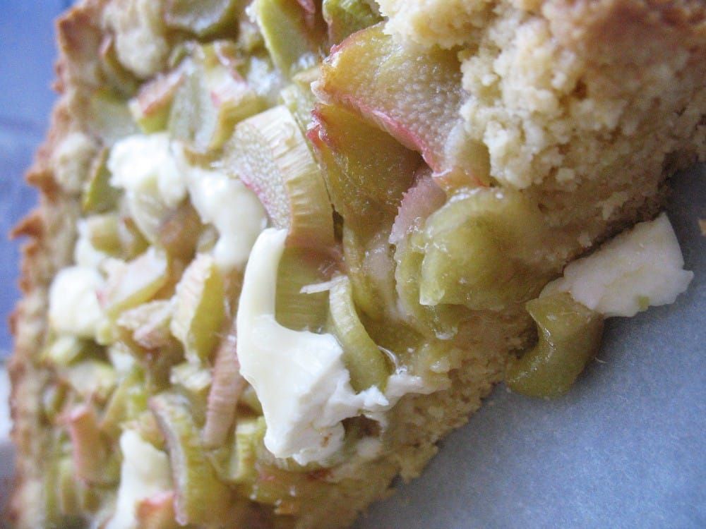 Nahaufnahme eines saftigen Rhabarberkuchens mit Streuseln und grün-rosa Rhabarberstücken