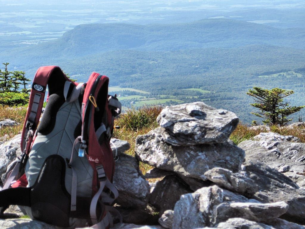 Roter und grauer Wanderrucksack auf einem Felsen am Gipfel mit Blick über bewaldete Hügel und Täler