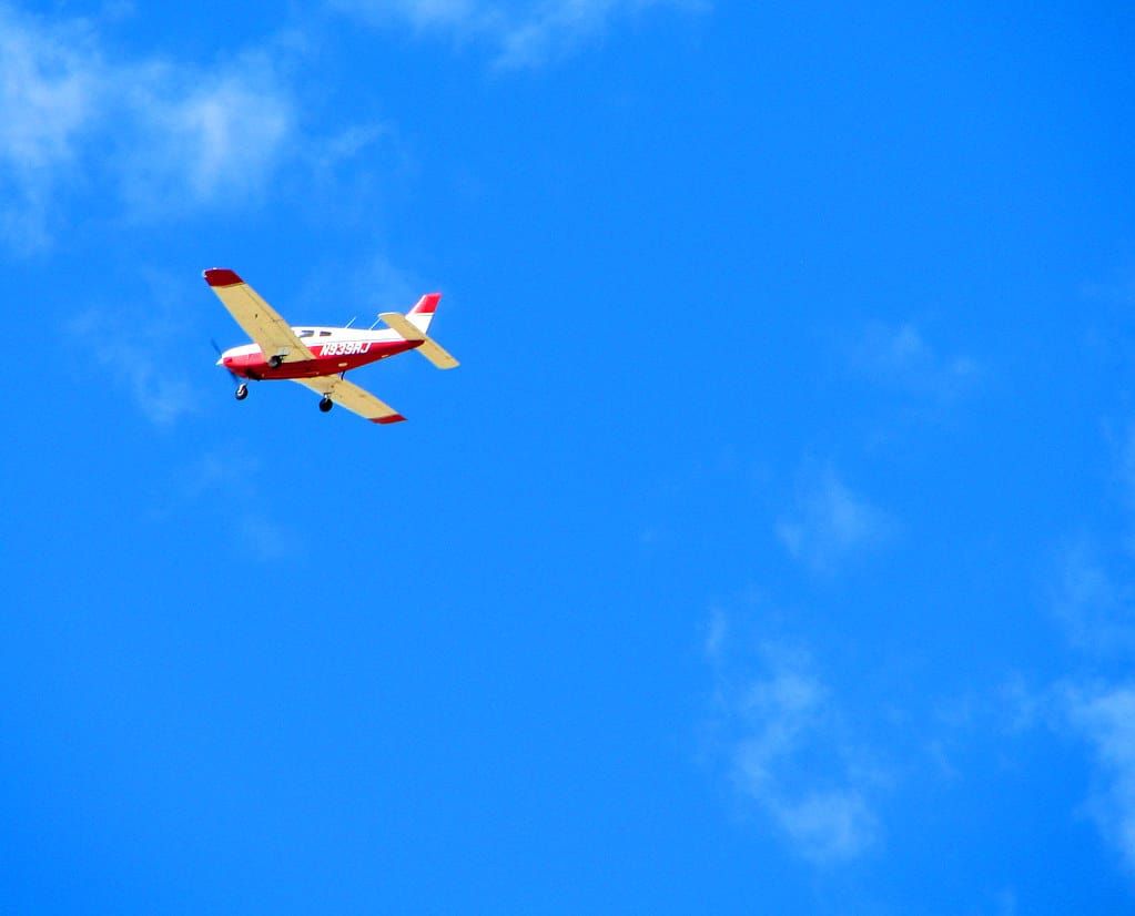 Rot-weißes einmotoriges Kleinflugzeug im Flug vor strahlend blauem Himmel mit wenigen Wolken