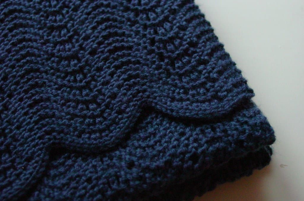 Nahaufnahme eines dunkelblauen, fein gestrickten Schals mit welligem Muster auf hellem Untergrund