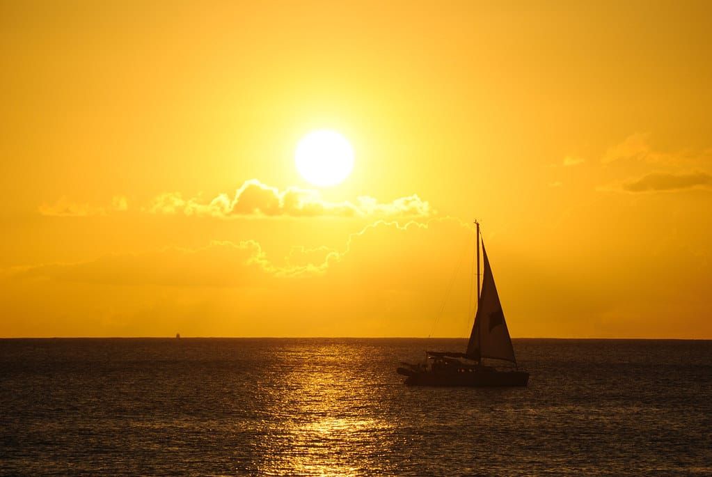 Silhouette eines Segelboots auf dem Meer vor tief stehender Sonne und goldgelbem Himmel