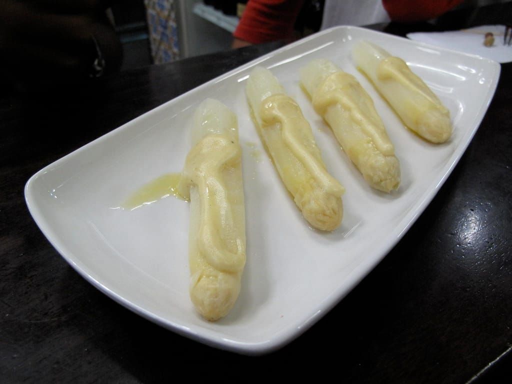 Vier Stangen weißer Spargel mit heller Soße auf einer länglichen weißen Porzellanplatte