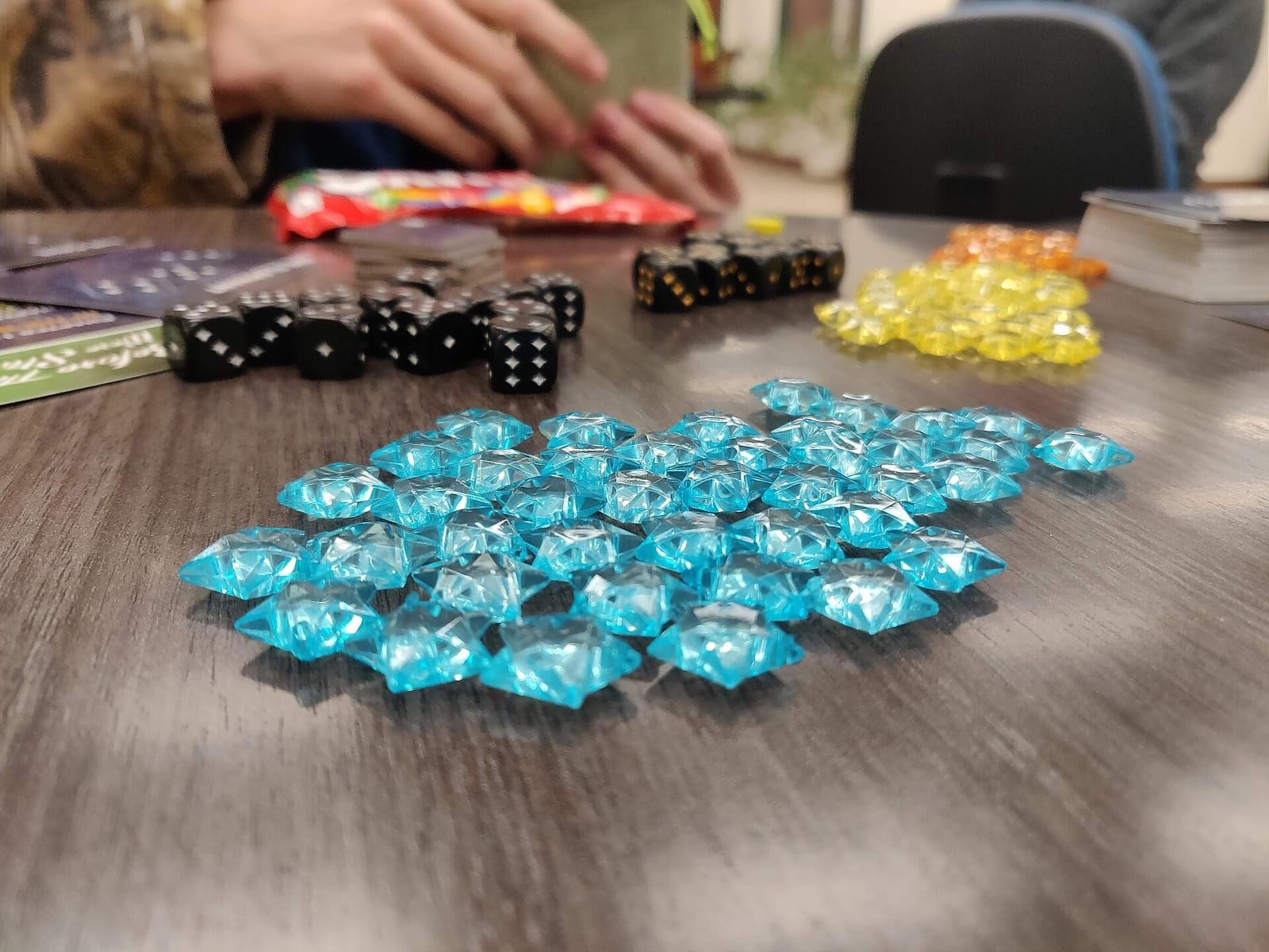 Spielsteine in Form blauer Kristalle, gelbe Steine und schwarze Würfel auf einem Holztisch