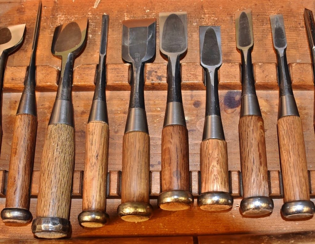 Reihe von Stechbeiteln mit Holzgriffen und Metallringen in einer hölzernen Halterung