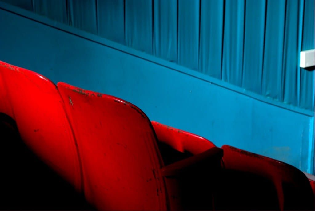 Rote Klappsitze in einem Saal vor einer blauen Wand mit blauem Vorhang