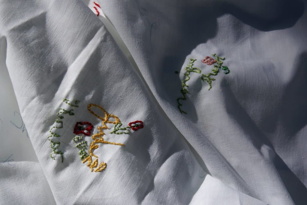 Weiße Stofftischdecke mit gestickten Namenszügen in Gelb und Grün und kleinen roten Blumen