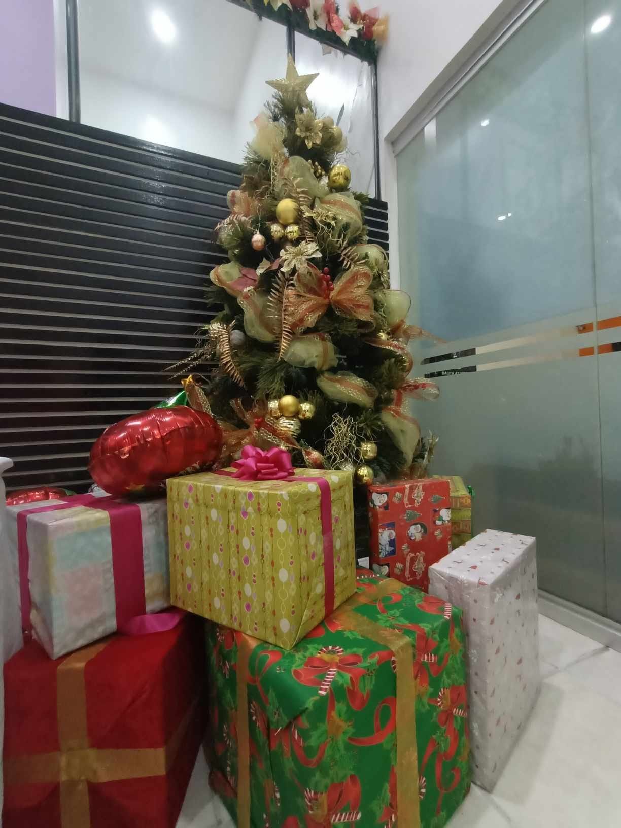 Geschmückter Weihnachtsbaum mit goldenen Kugeln, davor bunt verpackte Geschenke mit Schleifen