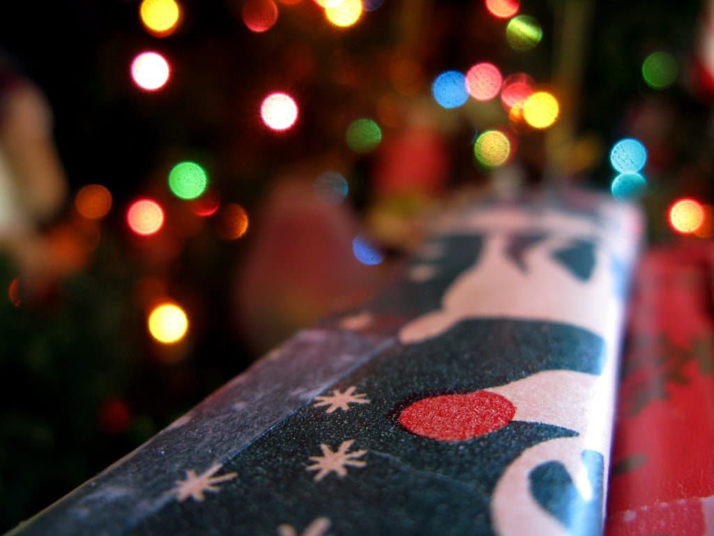 Nahaufnahme eines Geschenks in dunkelblauem Weihnachtspapier vor unscharf leuchtenden bunten Lichterketten
