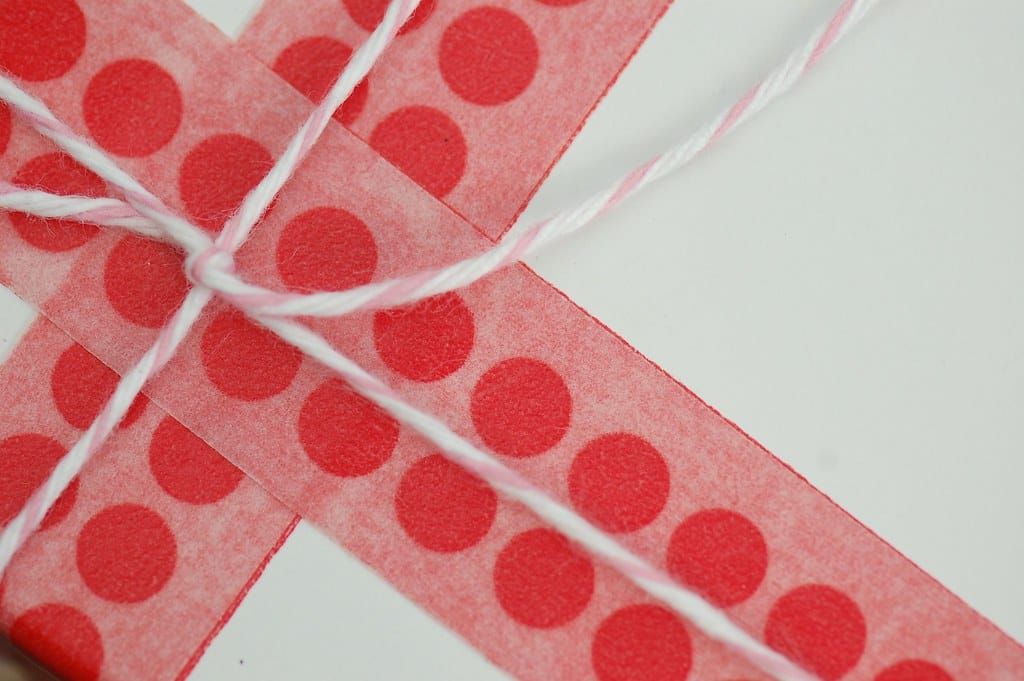 Geschenk in weißem Papier, umwickelt mit rot gepunktetem Band und rosa-weißer Kordel