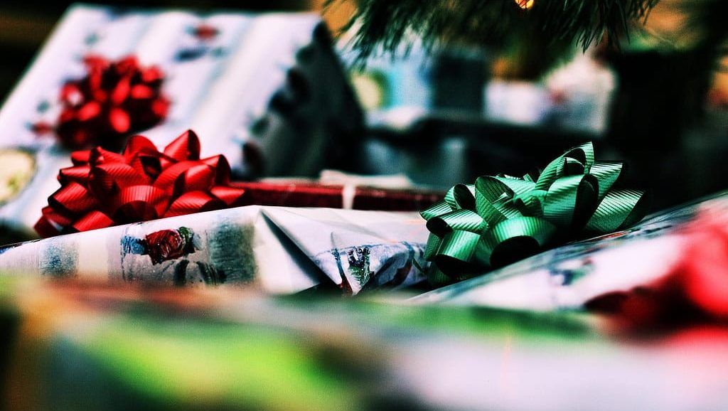 Eingepackte Weihnachtsgeschenke mit roten und grünen Schleifen unter den Zweigen eines Weihnachtsbaums